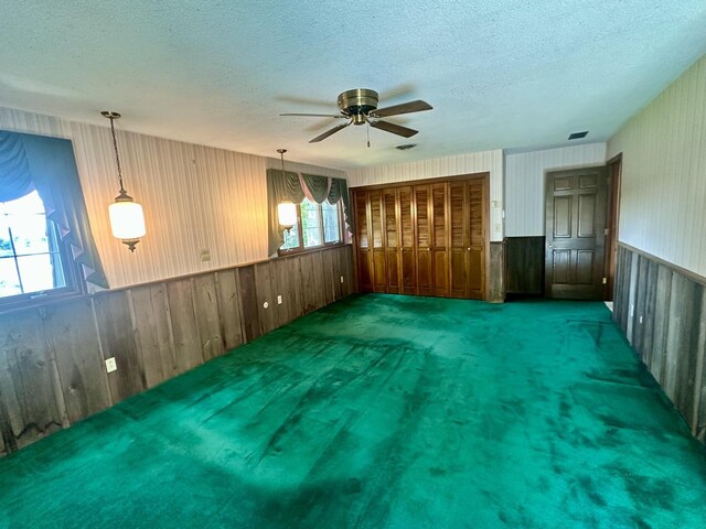 carpeted empty room featuring a wainscoted wall, a textured ceiling, visible vents, ceiling fan, and wallpapered walls