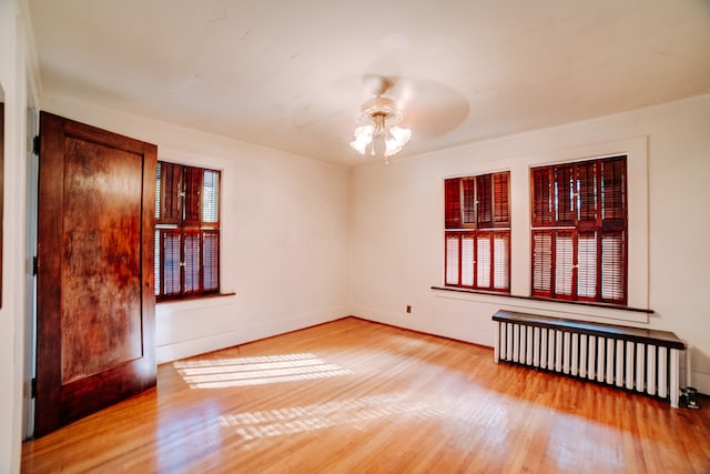 spare room featuring radiator heating unit, light hardwood / wood-style flooring, and ceiling fan