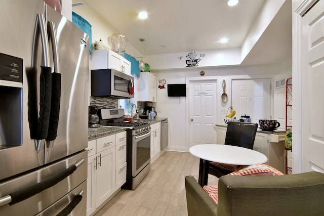 kitchen featuring decorative backsplash, white cabinets, dark stone countertops, light hardwood / wood-style floors, and stainless steel appliances