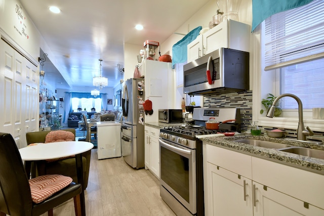 kitchen with stainless steel appliances, light wood-type flooring, tasteful backsplash, white cabinetry, and light stone counters