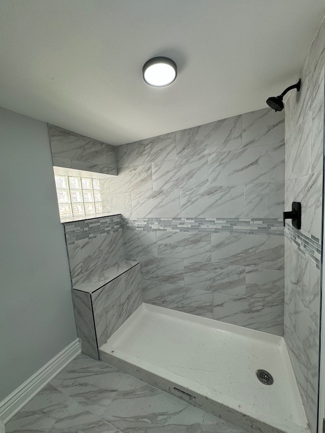 full bathroom featuring marble finish floor, a tile shower, and baseboards