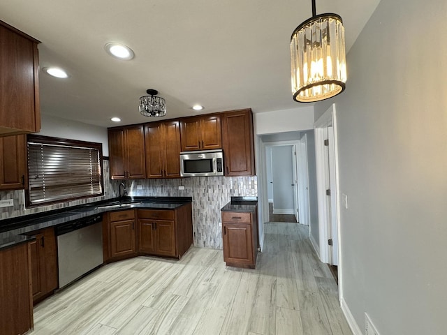 kitchen featuring stainless steel appliances, dark countertops, a notable chandelier, and decorative backsplash