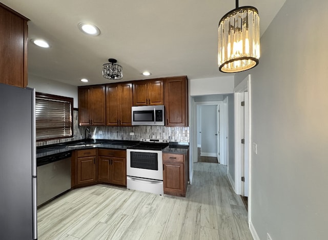 kitchen featuring a notable chandelier, a sink, appliances with stainless steel finishes, decorative backsplash, and dark countertops