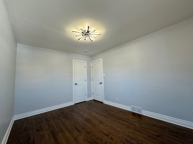 spare room featuring dark wood-style flooring, visible vents, and baseboards