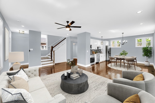 living room featuring ceiling fan with notable chandelier and dark wood-type flooring