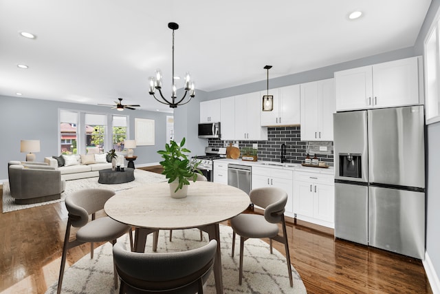 kitchen featuring appliances with stainless steel finishes, white cabinetry, dark hardwood / wood-style floors, pendant lighting, and ceiling fan with notable chandelier