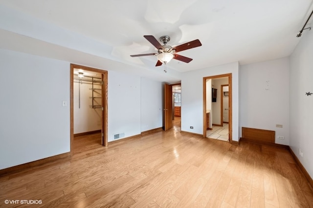 unfurnished bedroom featuring ceiling fan, ensuite bathroom, a walk in closet, light wood-type flooring, and a closet