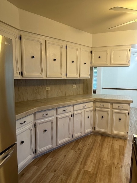 kitchen with light hardwood / wood-style flooring, ceiling fan, white cabinetry, stainless steel refrigerator, and backsplash