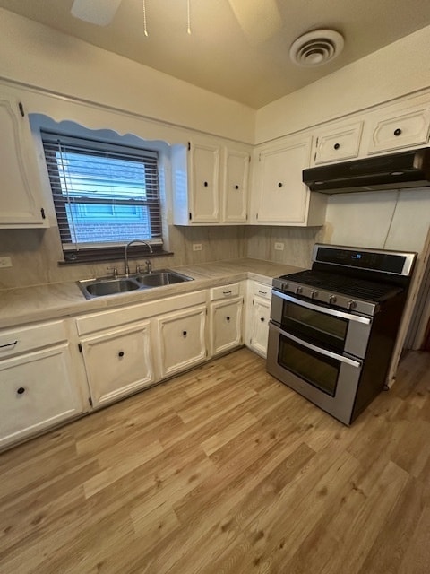 kitchen with range with two ovens, white cabinets, backsplash, sink, and light hardwood / wood-style floors