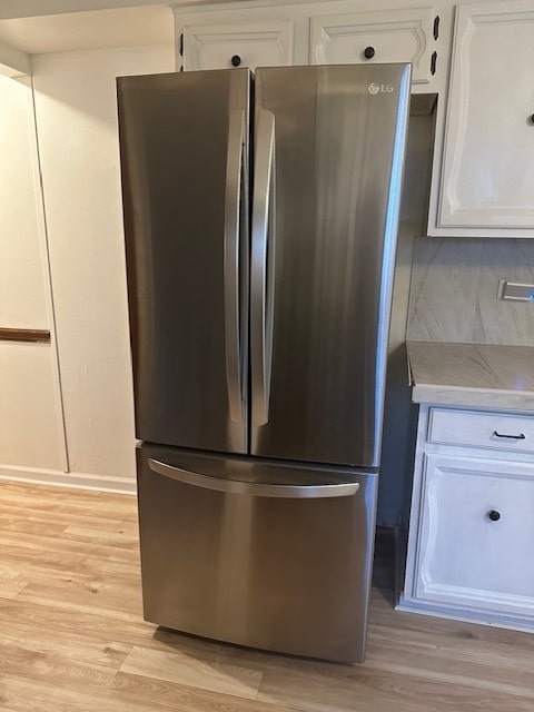 kitchen with stainless steel fridge, light hardwood / wood-style flooring, decorative backsplash, and white cabinetry