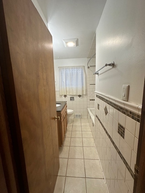 full bathroom with toilet, tile patterned flooring, tile walls, vanity, and shower / tub combination