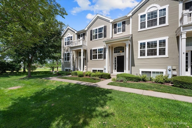 view of property featuring a balcony and a front lawn