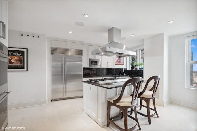 kitchen with island exhaust hood, plenty of natural light, built in appliances, and a breakfast bar