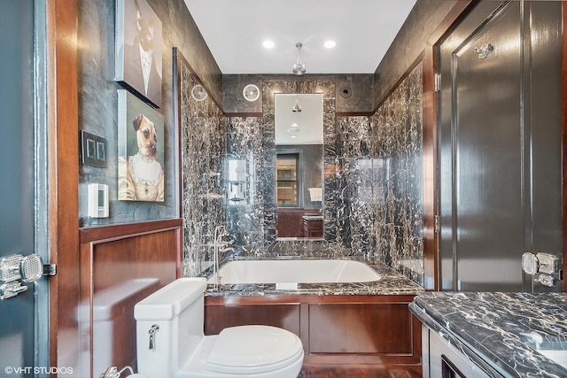 bathroom featuring tile walls, a tub to relax in, vanity, and toilet