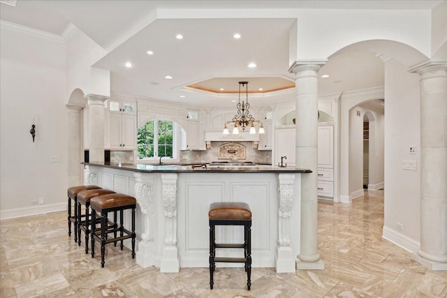 kitchen featuring white cabinetry, a kitchen bar, decorative light fixtures, and crown molding