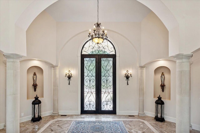 entryway with french doors, a towering ceiling, a chandelier, and ornate columns