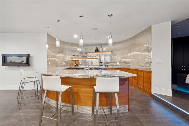 kitchen with a breakfast bar area, backsplash, hanging light fixtures, light stone countertops, and kitchen peninsula