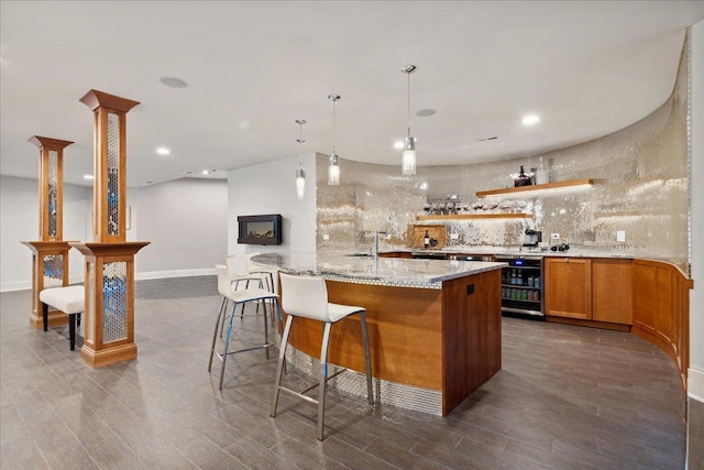 kitchen featuring dark wood-type flooring, light stone counters, a center island with sink, hanging light fixtures, and backsplash