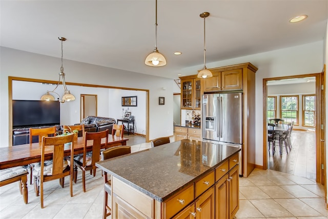 kitchen with stainless steel fridge with ice dispenser, light hardwood / wood-style floors, a center island, hanging light fixtures, and dark stone countertops