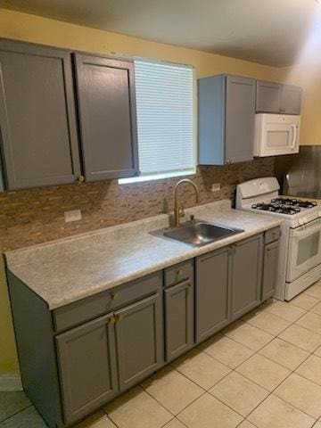 kitchen featuring backsplash, gray cabinetry, white appliances, sink, and light tile patterned floors