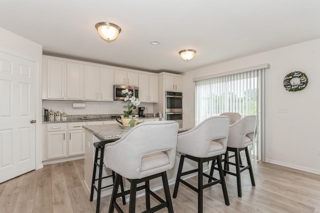 kitchen featuring a kitchen island with sink, light hardwood / wood-style flooring, a kitchen bar, appliances with stainless steel finishes, and white cabinets