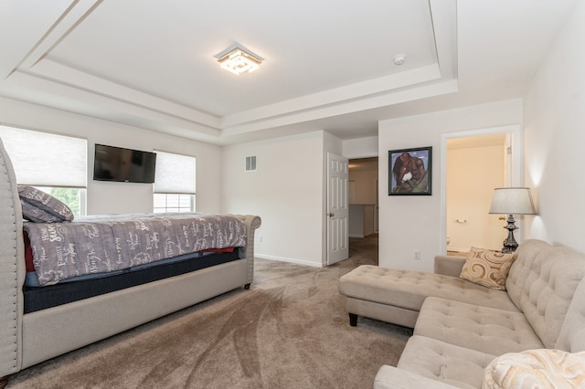 carpeted bedroom with a tray ceiling and ensuite bath