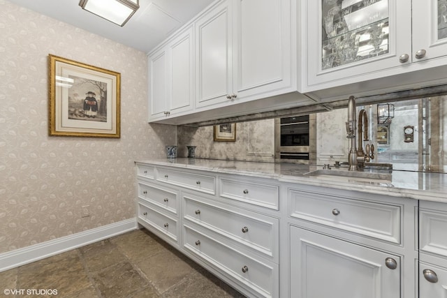 kitchen featuring light stone counters, sink, and white cabinets