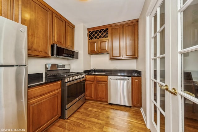 kitchen featuring a sink, light wood-style floors, appliances with stainless steel finishes, brown cabinets, and dark countertops