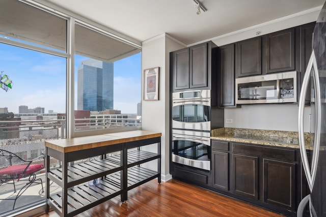 kitchen with appliances with stainless steel finishes, light stone counters, dark hardwood / wood-style floors, and a healthy amount of sunlight