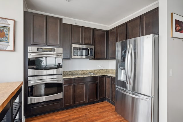 kitchen featuring hardwood / wood-style floors, dark brown cabinets, stainless steel appliances, and light stone counters