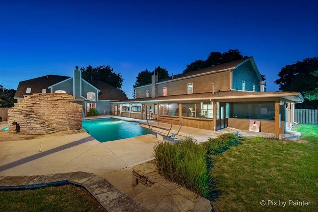 pool at night featuring a patio and a yard