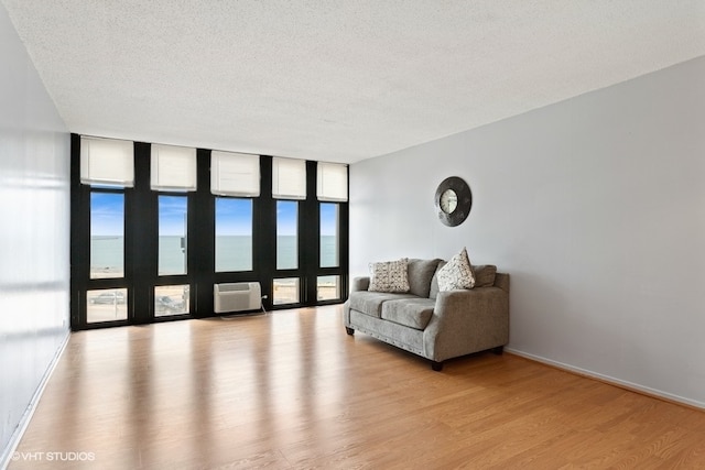 living area with a wall mounted AC, a textured ceiling, floor to ceiling windows, and light hardwood / wood-style floors