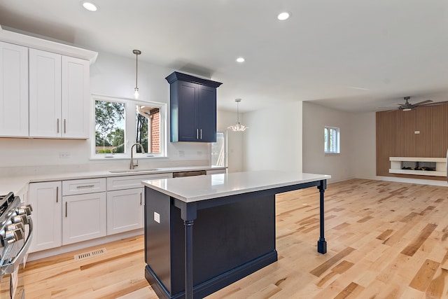 kitchen featuring light hardwood / wood-style flooring, stainless steel stove, hanging light fixtures, sink, and ceiling fan