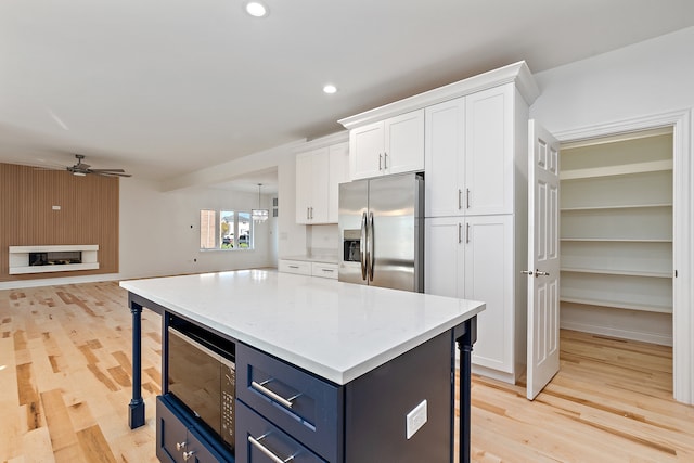 kitchen with light wood-type flooring, ceiling fan, stainless steel refrigerator with ice dispenser, black microwave, and white cabinets