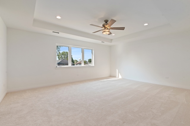 unfurnished room featuring a raised ceiling, light colored carpet, and ceiling fan