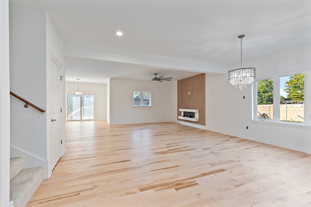 unfurnished living room featuring ceiling fan with notable chandelier, light wood-type flooring, and a fireplace