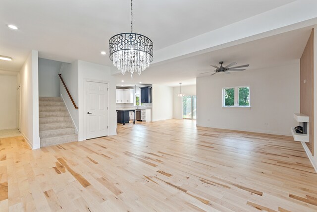 unfurnished living room featuring light wood-type flooring and ceiling fan with notable chandelier