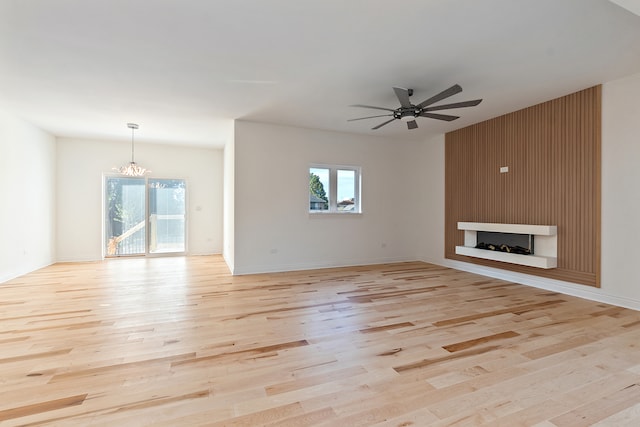 unfurnished living room featuring a large fireplace, ceiling fan with notable chandelier, and light hardwood / wood-style flooring