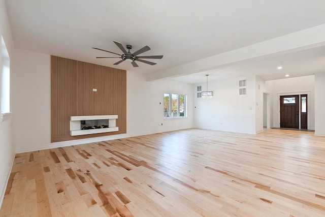 unfurnished living room featuring ceiling fan with notable chandelier, a fireplace, and light hardwood / wood-style floors