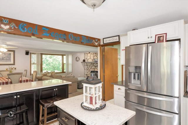 kitchen with white cabinetry, light stone counters, a center island, ceiling fan, and stainless steel fridge with ice dispenser