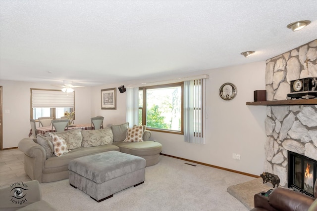 living room with a textured ceiling, a stone fireplace, ceiling fan, and light colored carpet