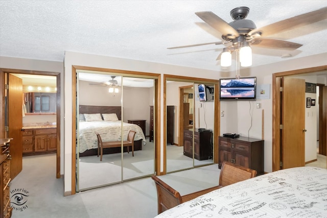 bedroom with ceiling fan, connected bathroom, sink, a textured ceiling, and two closets