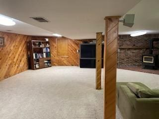 basement with carpet floors, wooden walls, and a wood stove