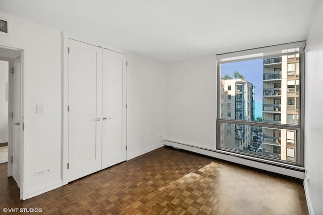 unfurnished bedroom with a baseboard heating unit and dark parquet flooring