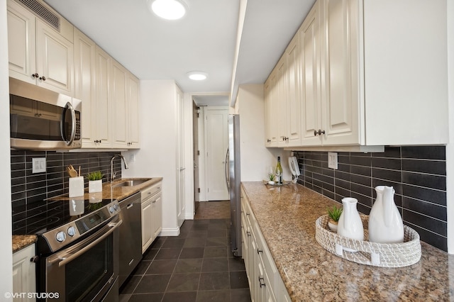 kitchen featuring appliances with stainless steel finishes, backsplash, dark tile patterned flooring, and sink