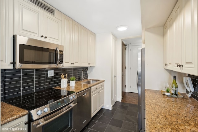 kitchen featuring tasteful backsplash, stainless steel appliances, dark tile patterned floors, white cabinets, and sink