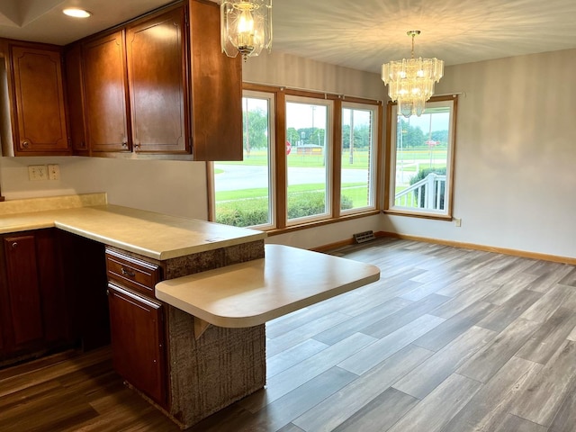 kitchen with dark hardwood / wood-style flooring, kitchen peninsula, a chandelier, decorative light fixtures, and a breakfast bar area