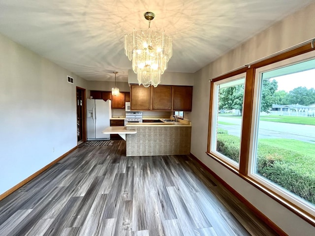 kitchen with white fridge with ice dispenser, dark hardwood / wood-style flooring, kitchen peninsula, pendant lighting, and a chandelier