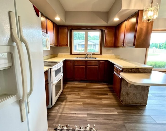 kitchen with kitchen peninsula, white appliances, sink, pendant lighting, and hardwood / wood-style floors