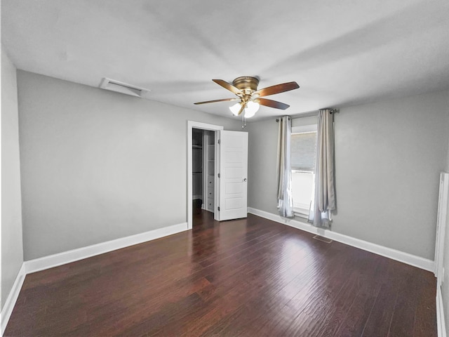 unfurnished bedroom with a closet, ceiling fan, a walk in closet, and dark hardwood / wood-style flooring